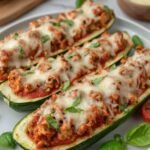Keto Chicken Parmesan Zucchini Boats topped with melted mozzarella and fresh basil on a baking sheet