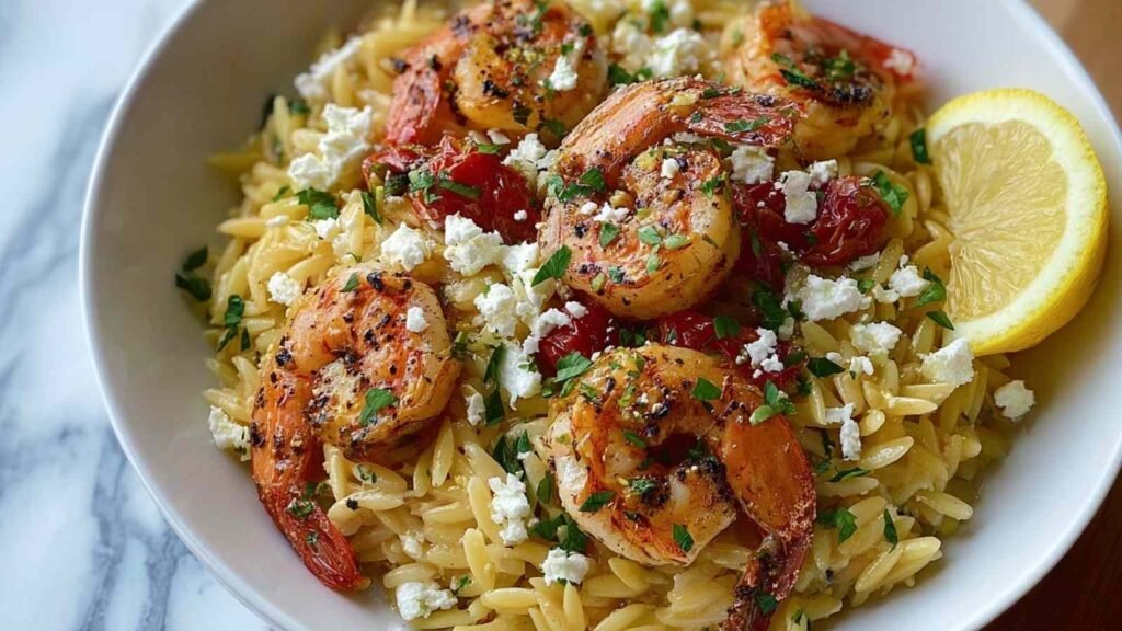 Close-up of Lemon Feta Orzo with Shrimp in a white bowl garnished with fresh parsley and a lemon wedge