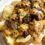 Loaded baked potato with steak topped with melted cheddar cheese, crumbled bacon, sour cream, and green onions on a rustic plate