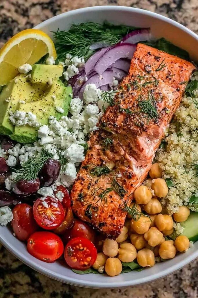 Mediterranean Salmon Bowl 8 Overhead view of a Mediterranean Salmon Bowl with flaky baked salmon, quinoa, cherry tomatoes, cucumber, olives, and feta drizzled with lemon herb dressing