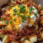 Overhead view of an air fryer loaded baked potato bowl topped with melted cheddar cheese, bacon bits, sour cream, and green onions