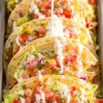 BBQ Ranch Chicken Tacos topped with shredded lettuce, diced tomatoes, and cheddar cheese on a wooden serving board