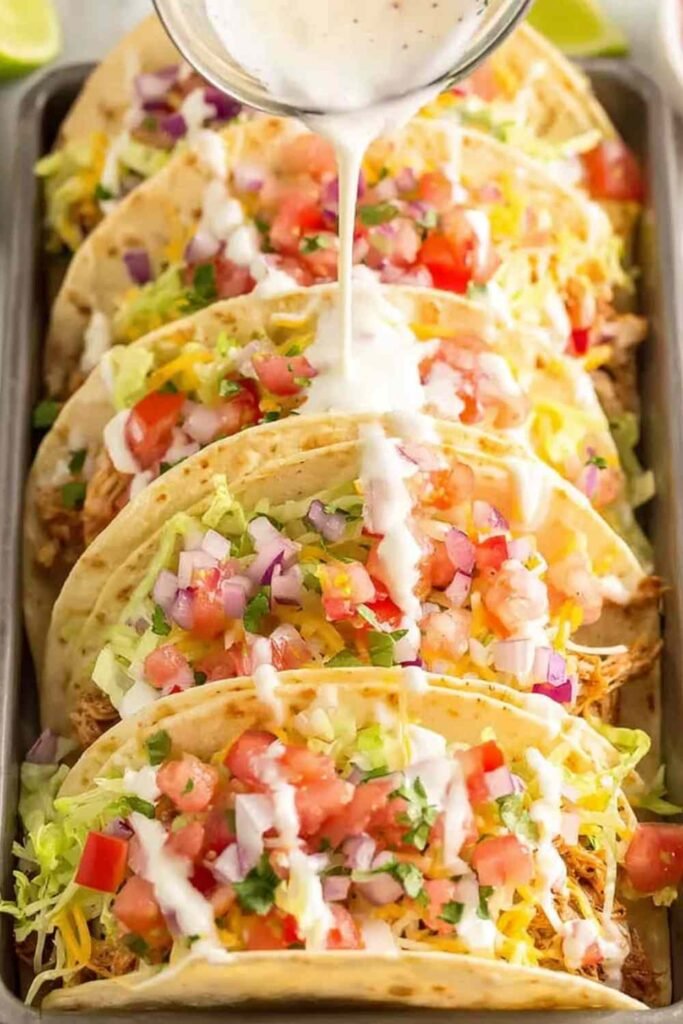 BBQ Ranch Chicken Tacos topped with shredded lettuce, diced tomatoes, and cheddar cheese on a wooden serving board