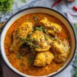 Badami Chicken Curry recipe served in a white bowl with a rich almond gravy garnished with cream and fenugreek leaves