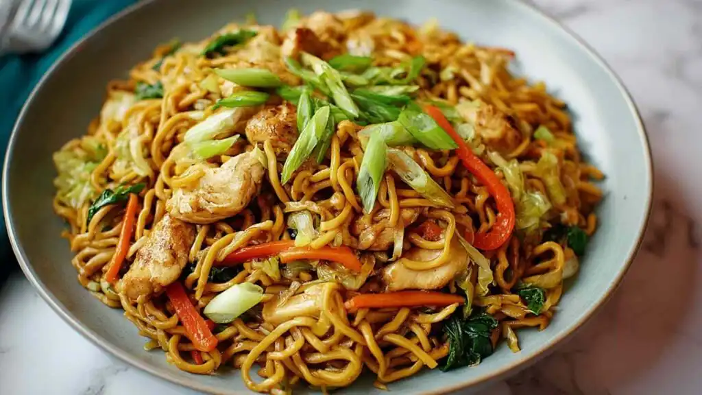 Chicken yakisoba in a large black skillet topped with sesame seeds and sliced green onions