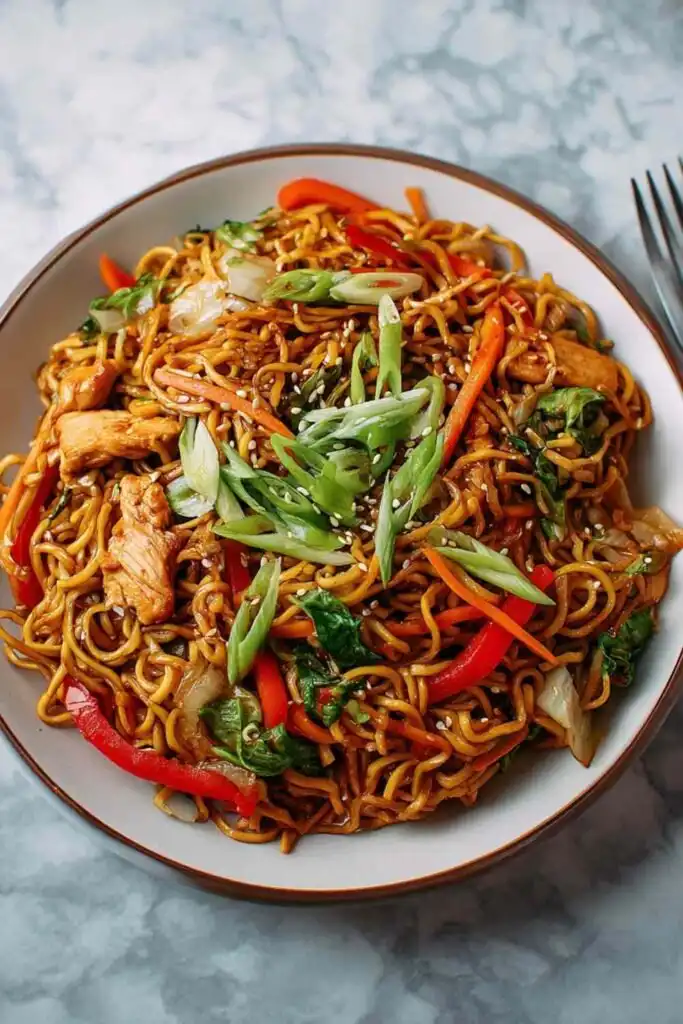 Chicken yakisoba in a large black skillet topped with sesame seeds and sliced green onions