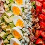 Overhead view of a classic Cobb salad recipe arranged in neat rows on a white platter with shallot vinaigrette on the side