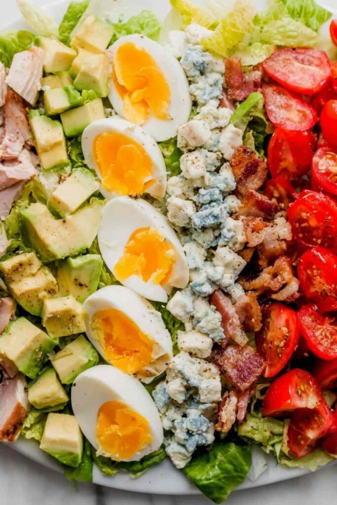 Overhead view of a classic Cobb salad recipe arranged in neat rows on a white platter with shallot vinaigrette on the side