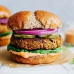 Classic lentil burgers on whole grain buns with avocado, tomato, and red onion on a wooden board