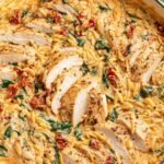 Creamy Tuscan Chicken Orzo 21 Creamy Tuscan chicken orzo in a cast iron skillet with sliced chicken, sun-dried tomatoes, and fresh basil garnish