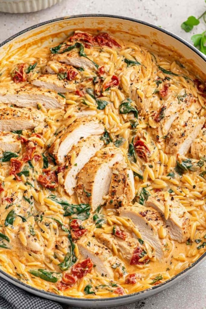 Creamy Tuscan Chicken Orzo 20 Creamy Tuscan chicken orzo in a cast iron skillet with sliced chicken, sun-dried tomatoes, and fresh basil garnish