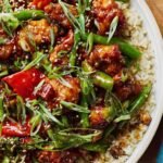 Homemade General Tso's Chicken in a skillet with sticky sweet and spicy sauce, garnished with green onions and sesame seeds