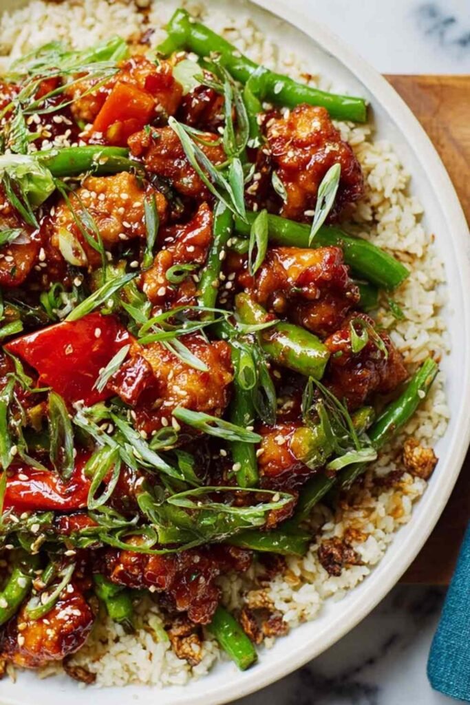 Homemade General Tso's Chicken in a skillet with sticky sweet and spicy sauce, garnished with green onions and sesame seeds