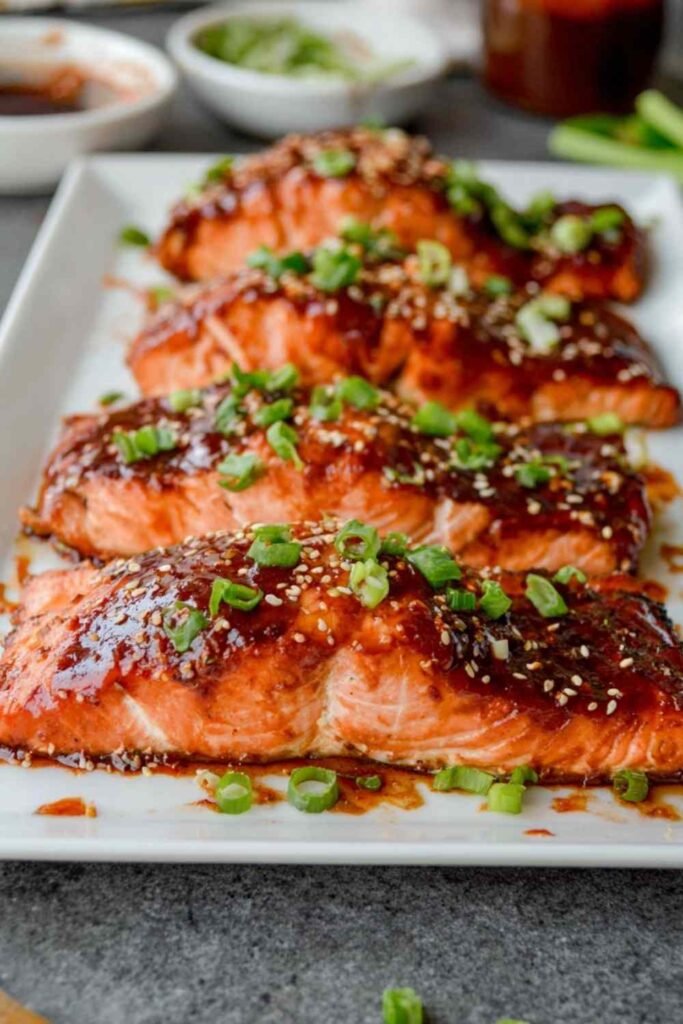 Gochujang Salmon 8 Broiled gochujang salmon fillets garnished with sesame seeds and green onion on a white plate