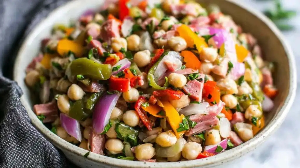 Grinder Dense Bean Salad with garbanzo beans, salami, pepperoncini, and bell peppers tossed in red wine vinaigrette in a large white bowl