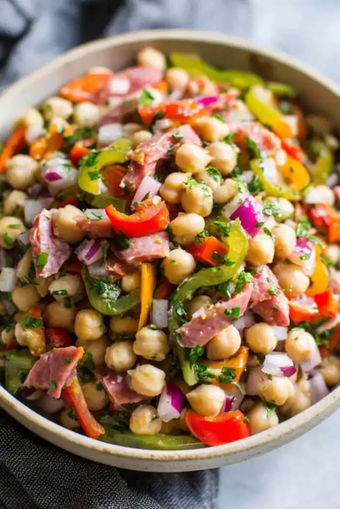 Grinder Dense Bean Salad with garbanzo beans, salami, pepperoncini, and bell peppers tossed in red wine vinaigrette in a large white bowl