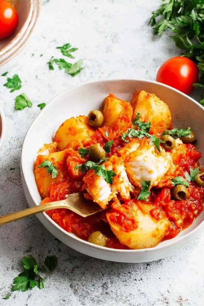 High Protein Bacalao a la Vizcaina served in a skillet with golden batter-fried salt cod, cannellini beans, potatoes, and green olives in tomato sauce