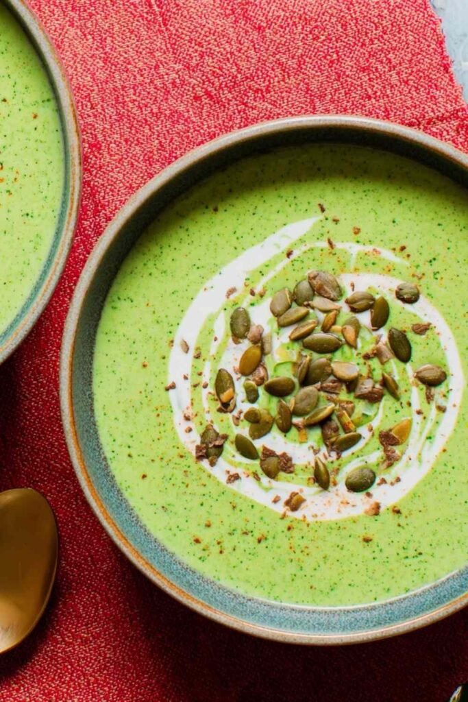 Overhead view of high protein broccoli cheddar soup in a white bowl topped with shredded cheddar