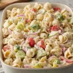 Overhead view of a high protein ranch pasta salad with shredded chicken, chickpea pasta, and fresh vegetables in a white bowl