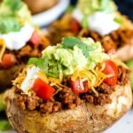 Taco Potatoes 30 Loaded taco potatoes topped with seasoned ground beef, shredded cheddar, sour cream, and fresh vegetables on a rustic plate