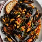 Mussels with cannellini beans and tomatoes in a large skillet with rich tomato white wine broth and fresh parsley garnish