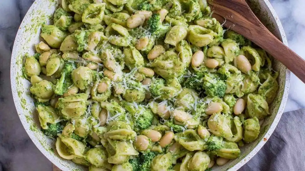High protein pesto pasta with broccoli and white beans served in a large white bowl with fresh lemon wedges on the side