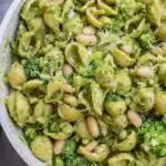 High protein pesto pasta with broccoli and white beans served in a large white bowl with fresh lemon wedges on the side