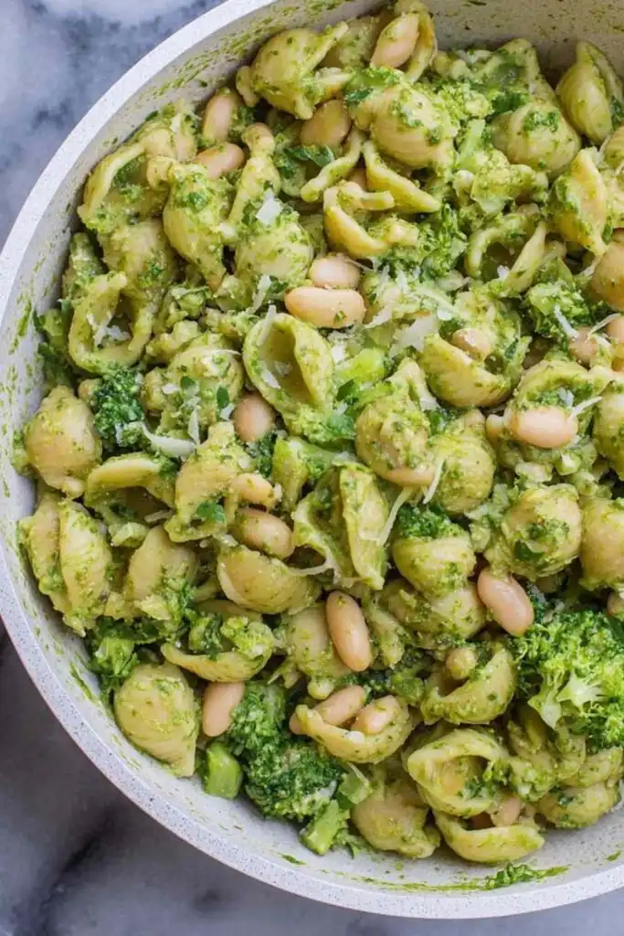 High protein pesto pasta with broccoli and white beans served in a large white bowl with fresh lemon wedges on the side