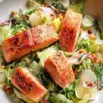 Overhead view of salmon and fennel dinner salad with seared salmon fillet, sliced avocado, thinly sliced fennel, and roasted almonds on mixed greens with lemon vinaigrette