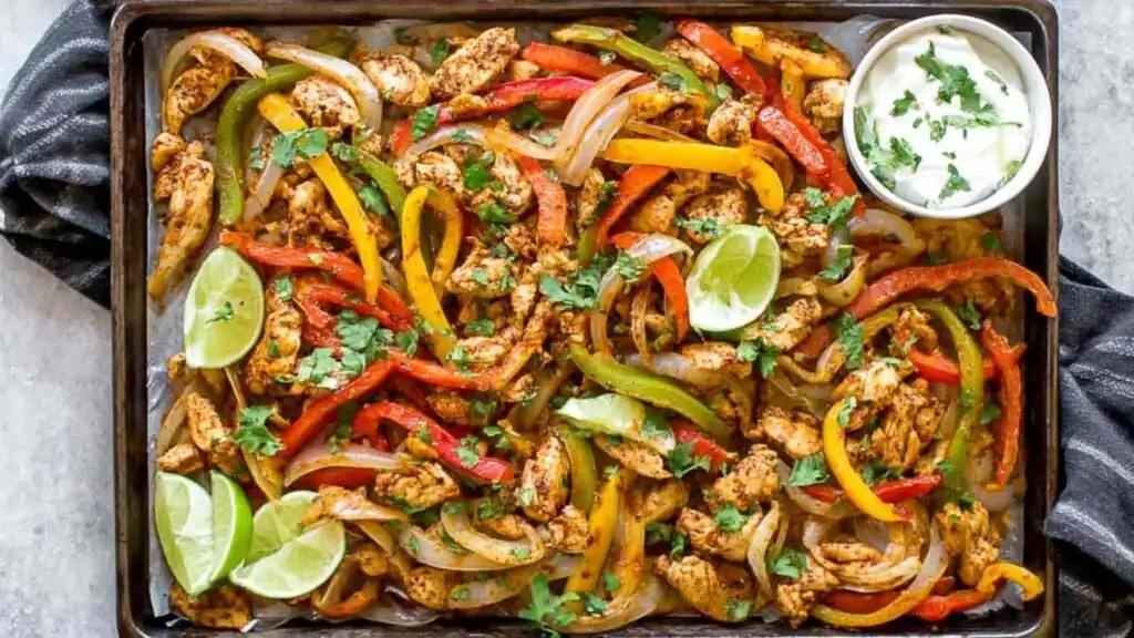 Sheet Pan Chicken Fajitas 1 Sheet pan chicken fajitas with seasoned chicken strips, roasted red yellow and green bell peppers, and fresh cilantro on a large baking sheet