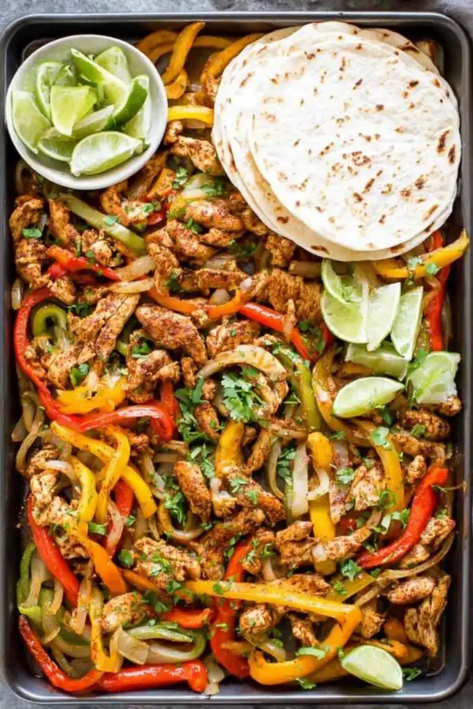 Sheet Pan Chicken Fajitas 2 Sheet pan chicken fajitas with seasoned chicken strips, roasted red yellow and green bell peppers, and fresh cilantro on a large baking sheet
