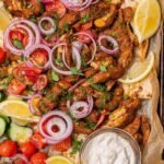 Sheet Pan Chicken Shawarma 27 Sheet pan chicken shawarma with roasted cherry tomatoes and red onion on a foil-lined baking sheet