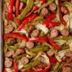 Sheet pan sausage and peppers with colorful roasted Italian sausage, red and yellow bell peppers, and red onion on a parchment-lined baking sheet