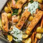 Overhead view of salmon and asparagus spring traybake with spiced mayo glaze, baby new potatoes, and fresh coriander on a baking tray