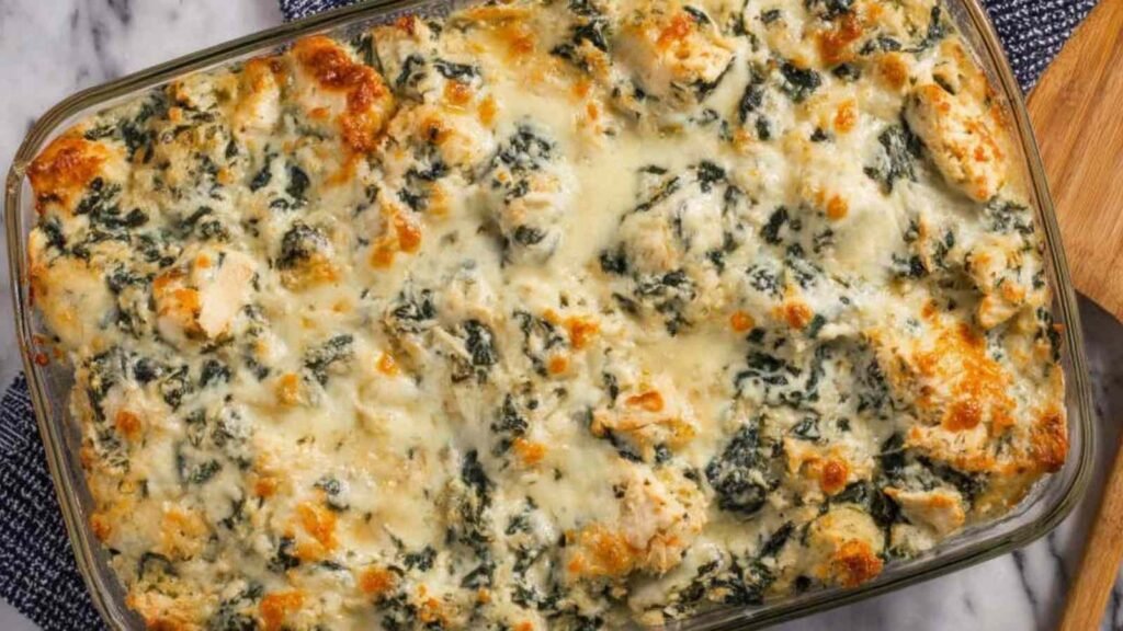 Spinach and artichoke chicken casserole in a white baking dish with golden melted mozzarella on top