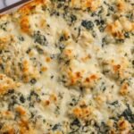 Spinach and artichoke chicken casserole in a white baking dish with golden melted mozzarella on top