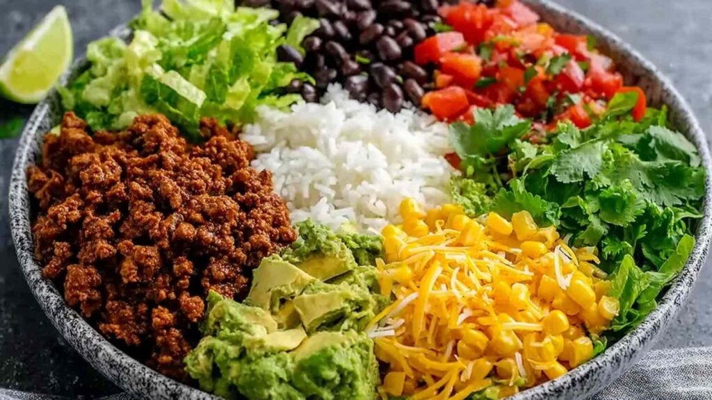 Taco rice bowl with black beans and avocado topped with shredded cheese, sour cream, and fresh cilantro