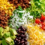 Taco rice bowl with black beans and avocado topped with shredded cheese, sour cream, and fresh cilantro