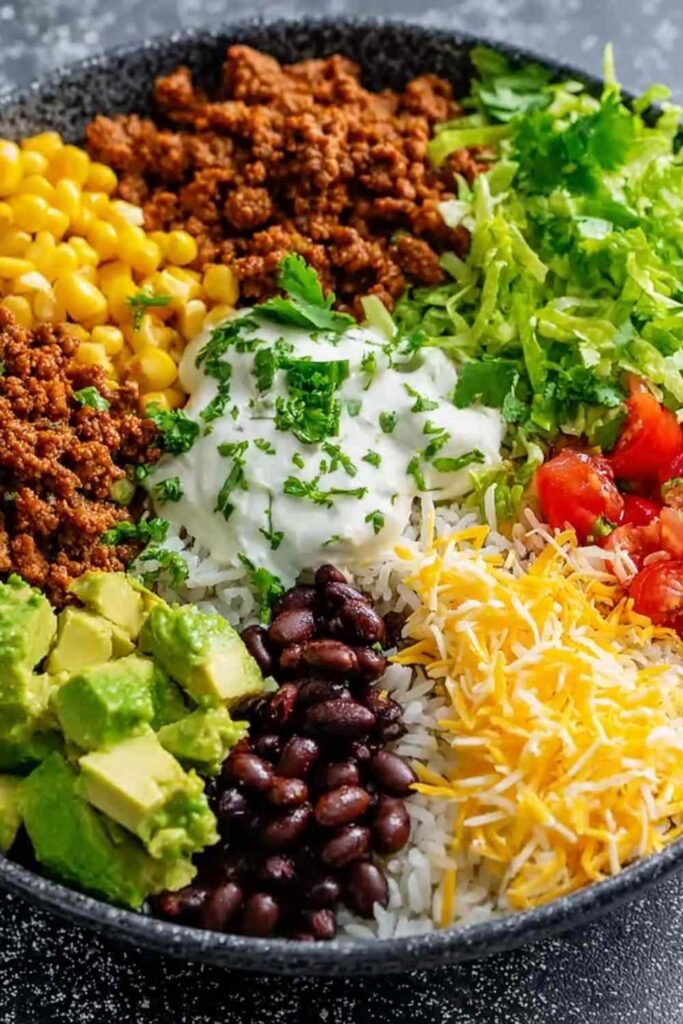 Taco rice bowl with black beans and avocado topped with shredded cheese, sour cream, and fresh cilantro