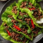Overhead view of Thai Basil Beef Lettuce Cups on a wooden board with fresh basil and lime wedges
