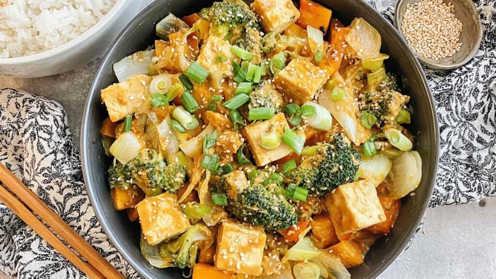 Tofu Vegetable Stir-Fry with Peanut Sauce 1 Crispy tofu vegetable stir-fry with peanut sauce in a large skillet garnished with sesame seeds and green onion