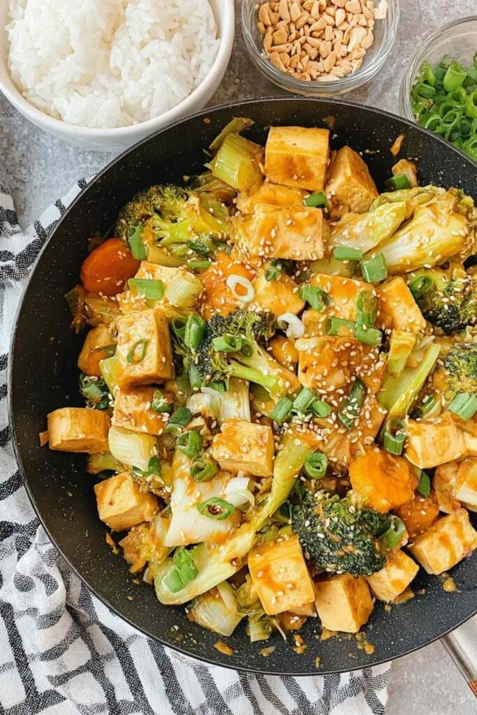 Tofu Vegetable Stir-Fry with Peanut Sauce 2 Crispy tofu vegetable stir-fry with peanut sauce in a large skillet garnished with sesame seeds and green onion