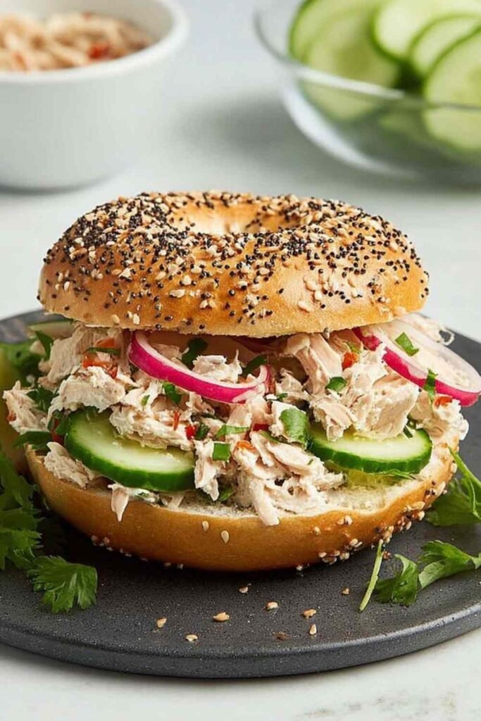 Tuna Everything Bagel 23 Close-up of a fully assembled tuna everything bagel with creamy herb tuna salad, red onion, tomato, cucumber, and Bibb lettuce on a toasted bagel with cream cheese
