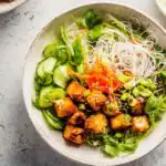 Close-up of a Vietnamese chicken noodle bowl with sliced lemongrass chicken, vermicelli, fresh herbs, and nuoc mam cham dressing
