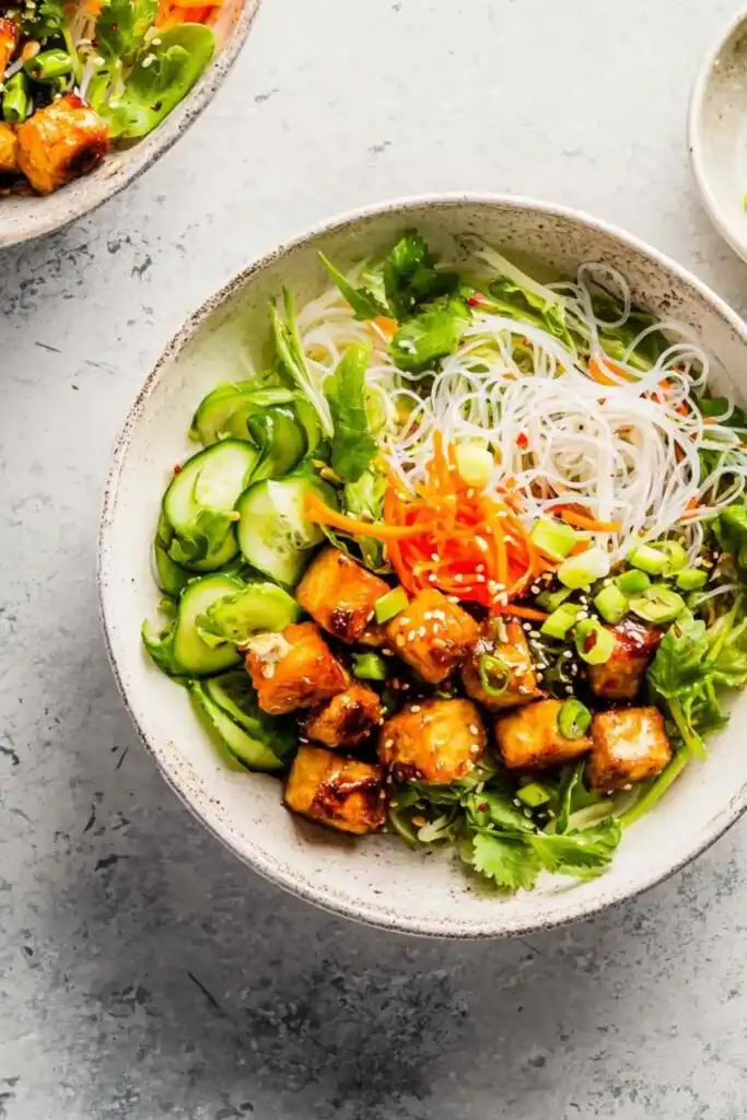 Close-up of a Vietnamese chicken noodle bowl with sliced lemongrass chicken, vermicelli, fresh herbs, and nuoc mam cham dressing
