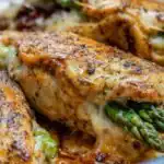 Asparagus Stuffed Chicken Breast 12 Golden seared asparagus stuffed chicken breast sliced open to reveal melty mozzarella and sun-dried tomatoes on a white plate