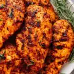 Sliced baked brown sugar chicken breast served over white rice with fresh herbs on a white plate
