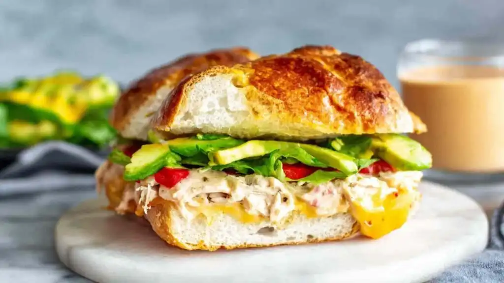 Close-up of a Chipotle Chicken Avocado Melt cut in half showing melted smoked Gouda, shredded chicken, avocado, and roasted red peppers on focaccia