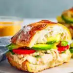 Close-up of a Chipotle Chicken Avocado Melt cut in half showing melted smoked Gouda, shredded chicken, avocado, and roasted red peppers on focaccia