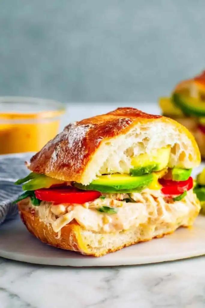 Close-up of a Chipotle Chicken Avocado Melt cut in half showing melted smoked Gouda, shredded chicken, avocado, and roasted red peppers on focaccia